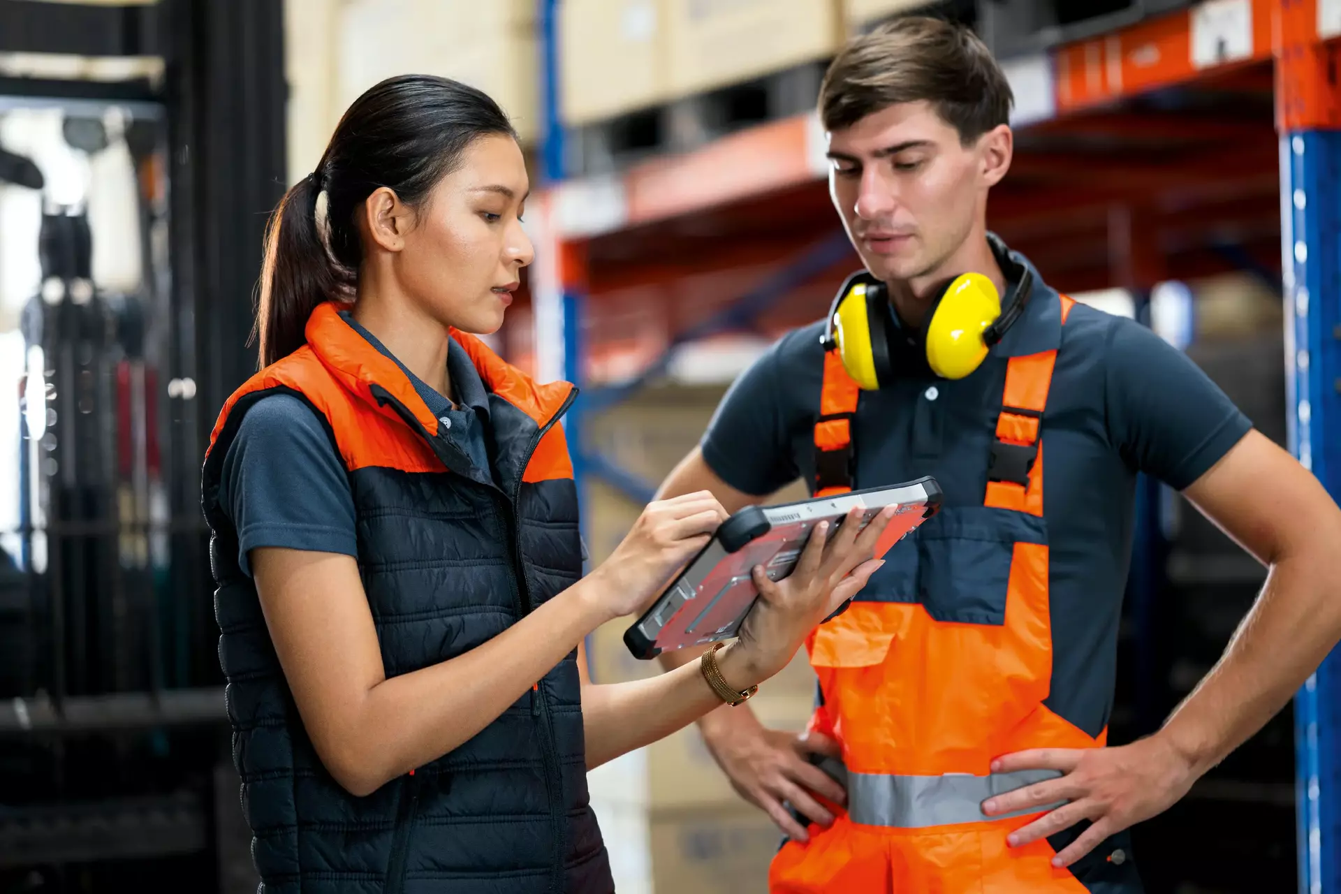 Female warehouse supervisor holding an industrial tablet while discussion with a forkflift driver