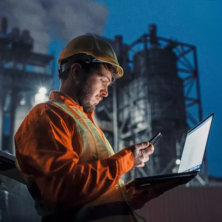 Engineer working nightshift and using technology in front of petroleum industrial factory