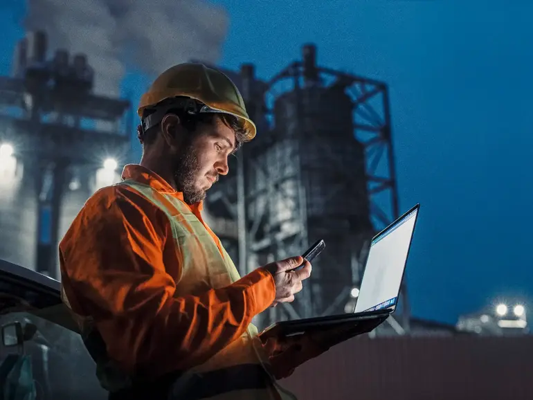 Engineer working nightshift and using technology in front of petroleum industrial factory
