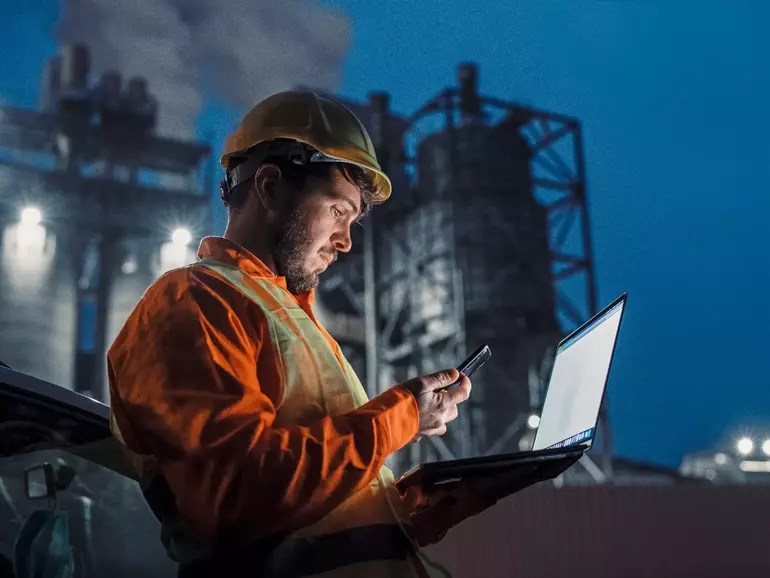 Engineer working nightshift and using technology in front of petroleum industrial factory