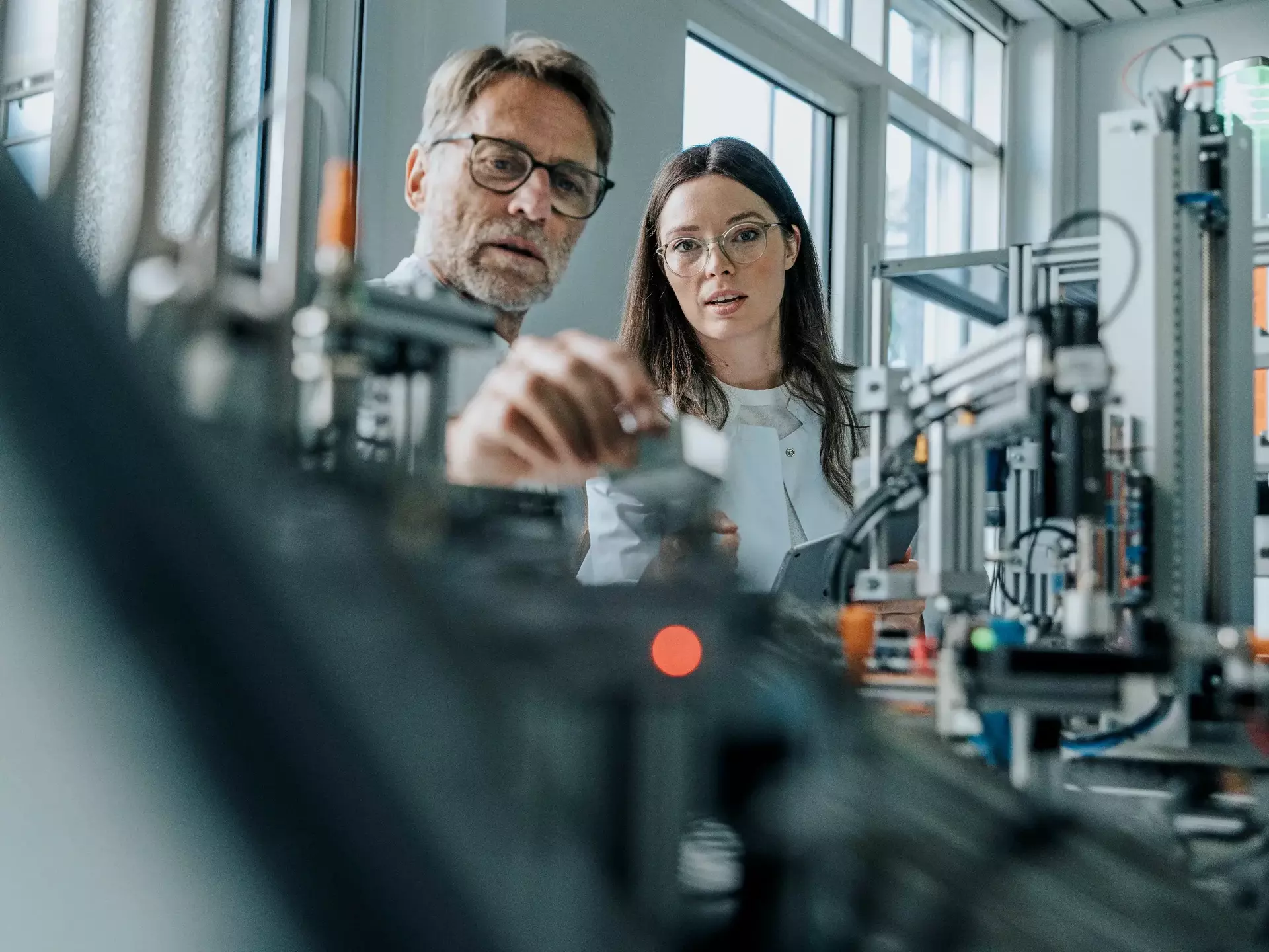 Male scientist with young woman examining machinery in laboratory