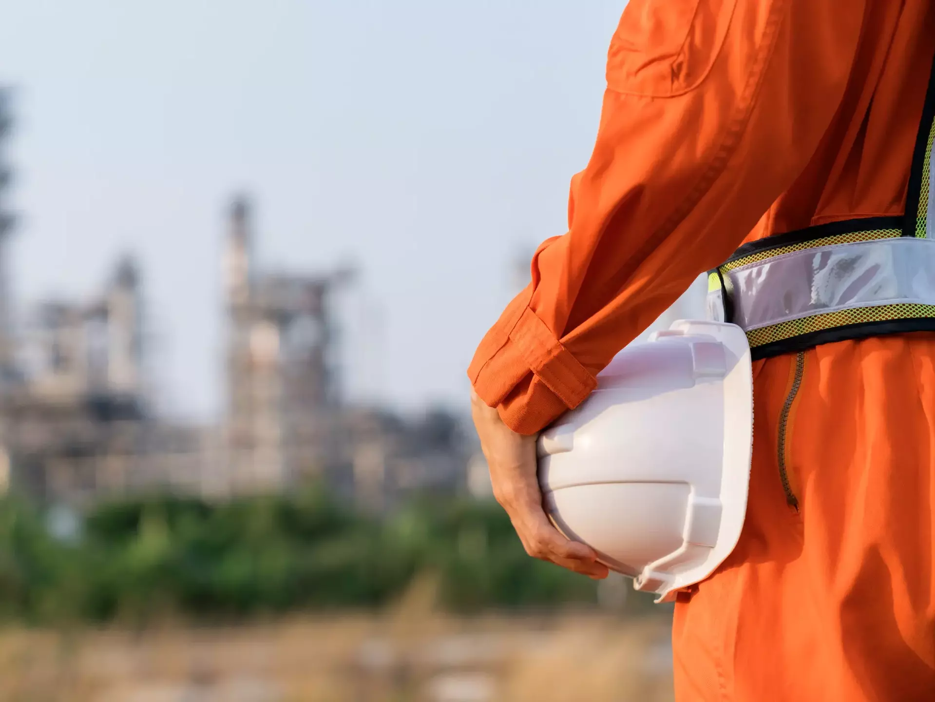 Rückansicht eines Ingenieurs, der einen weißen Sicherheitshelm trägt und den Hintergrund einer Ölraffinerie verwischt
