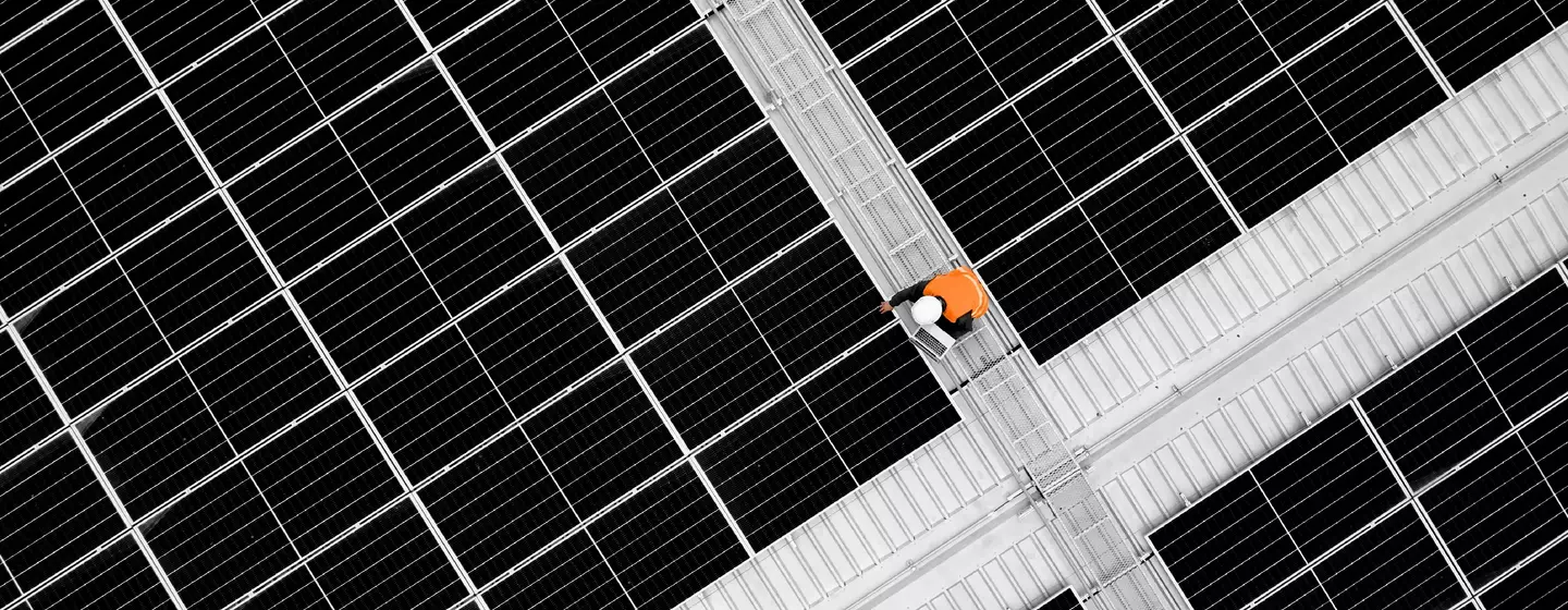 Blick von oben auf einen Ingenieur, der ein digitales Tablet hält, um die Daten eines Photovoltaiksystems während der Installation auf dem Dach zu analysieren