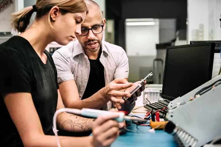 Techniker, der eine weibliche Auszubildende in der Werkstatt anleitet