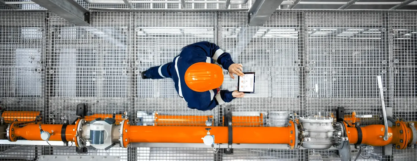 Mann, der auf einer Ölförderplattform einer Raffinerie arbeitet und neben einer Pipeline läuft
