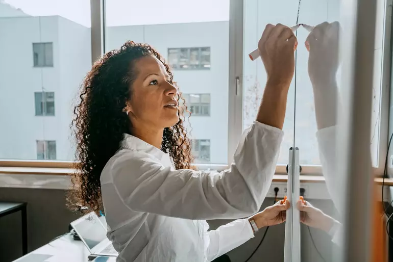 Side view of woman writing on whiteboard with felt tip pen in classroom