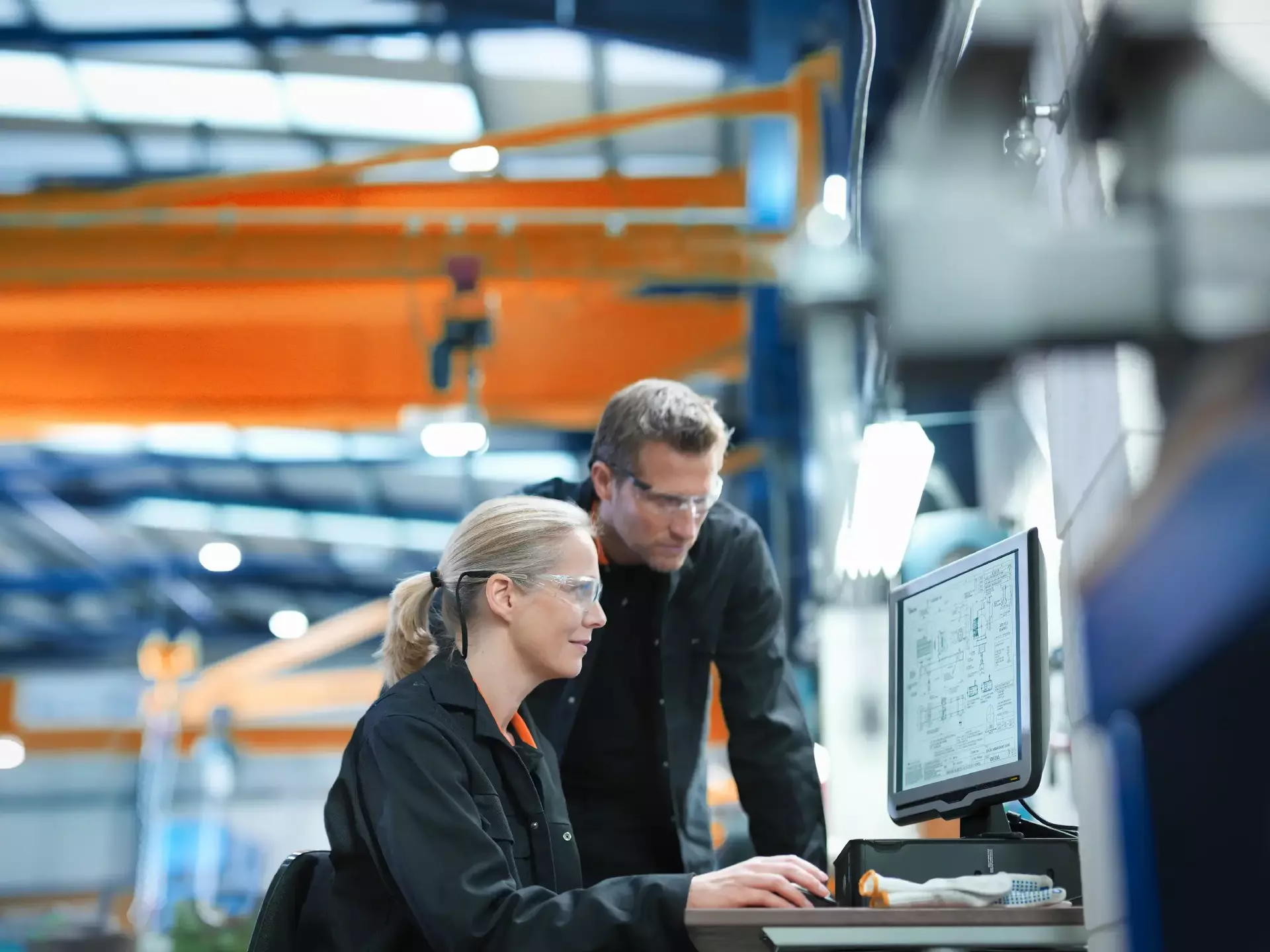 Engineers using computer to work on plans in engineering factory