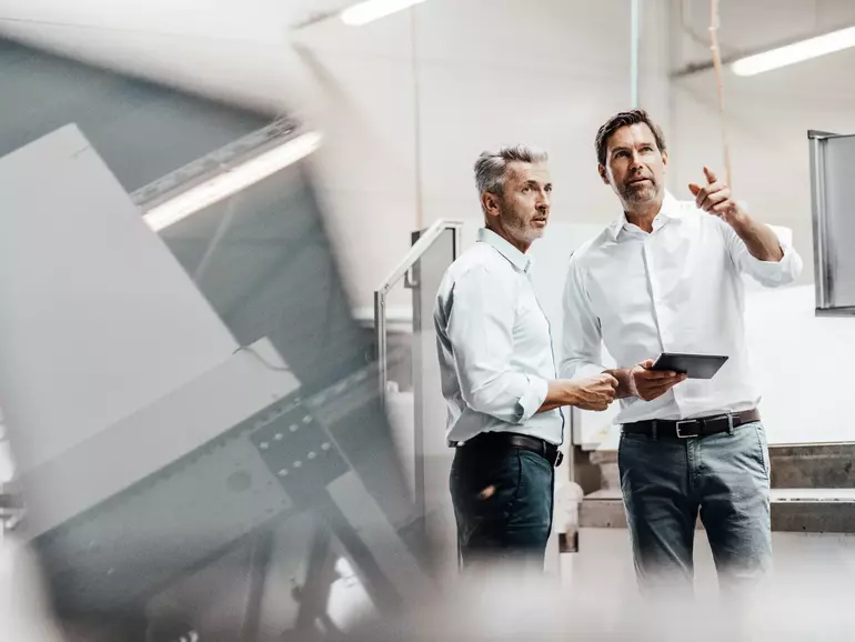 Male engineer with digital tablet pointing while discussing with colleague in manufacturing industry