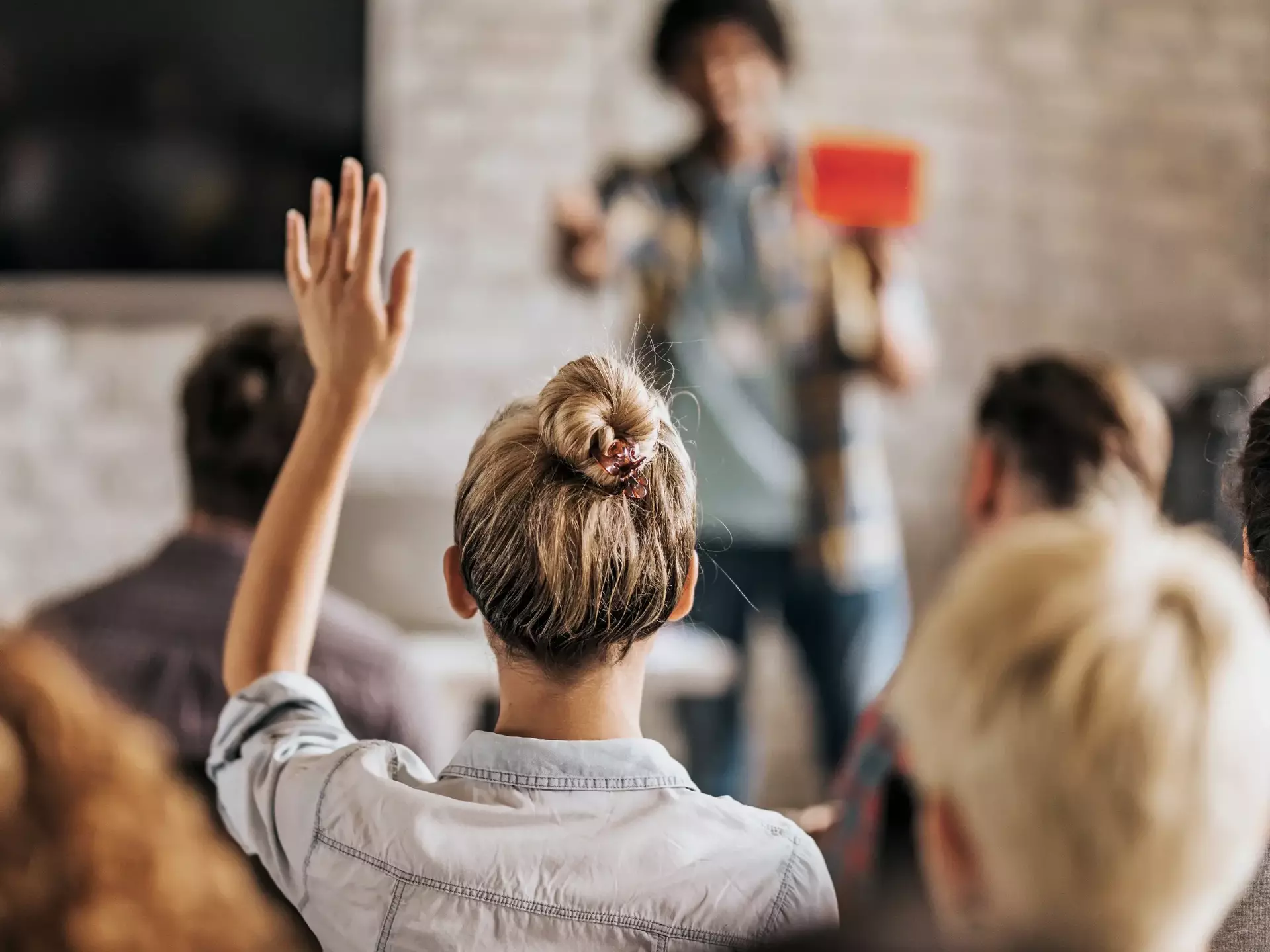 Rückenansicht einer Frau, die auf einem Seminar eine Frage stellen möchte