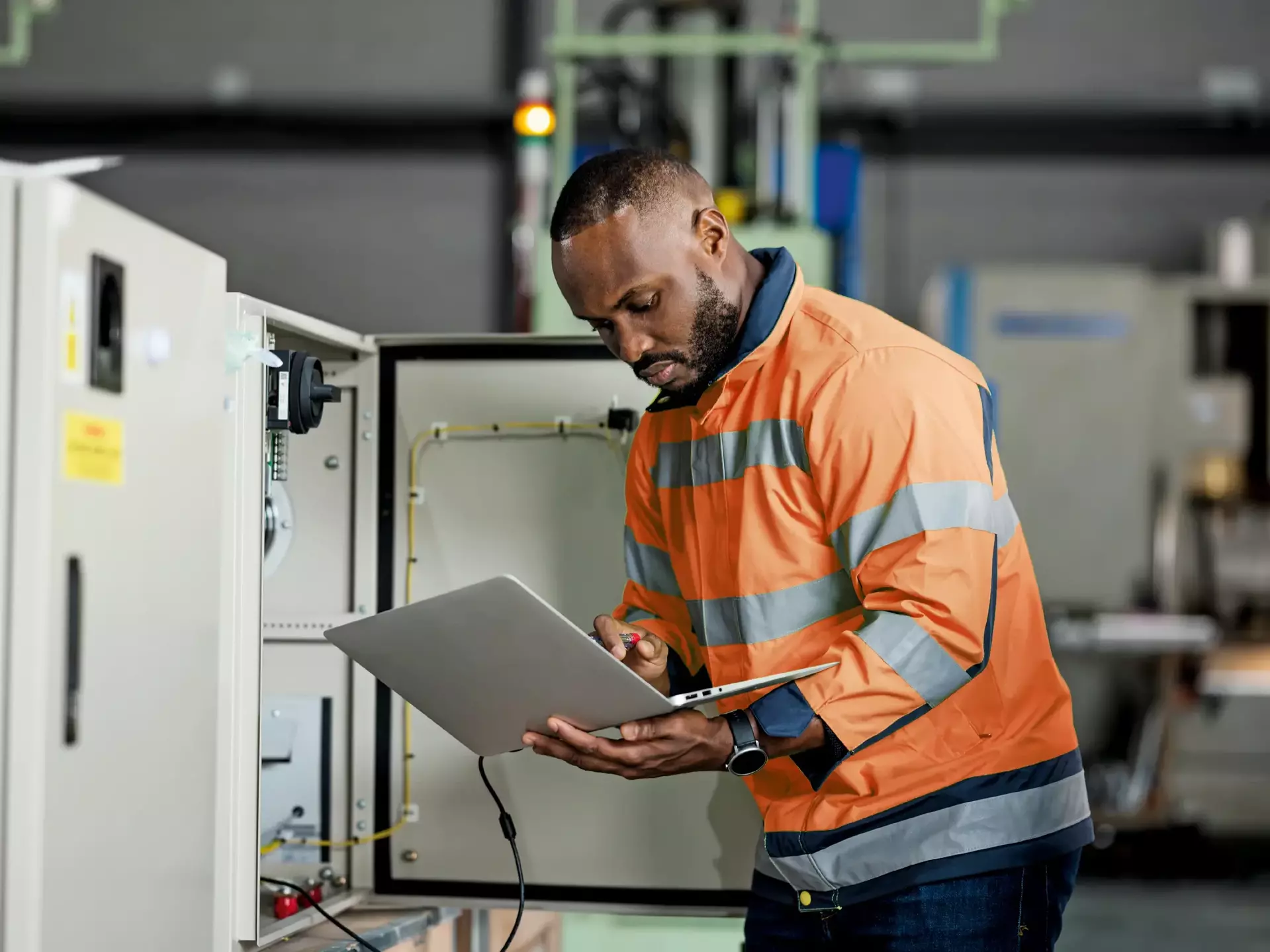 African electrician engineer is examining and testing complex equipment by a laptop in a circuit cabinet of the solar cell power storage