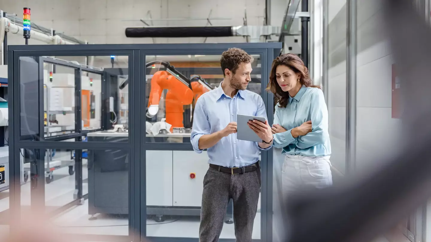 Two colleagues in high tech company talking next to industrial background