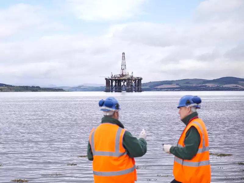 Two male oil worker on shore with oil rig in background
