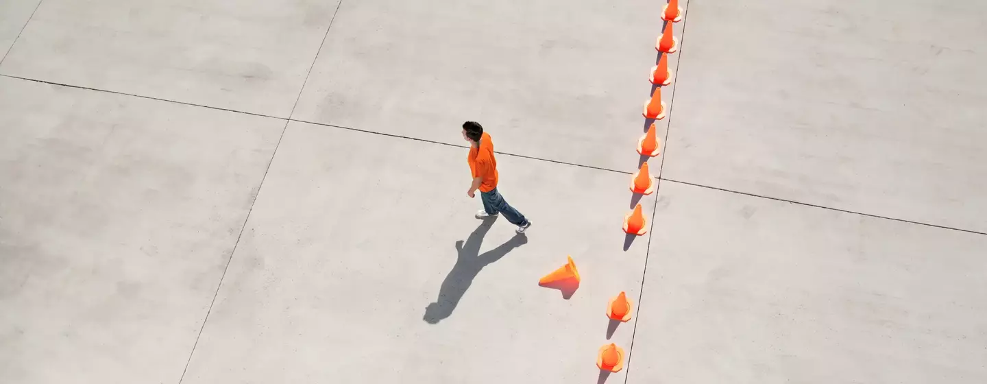 Man walking away from row of traffic cones with one misplaced